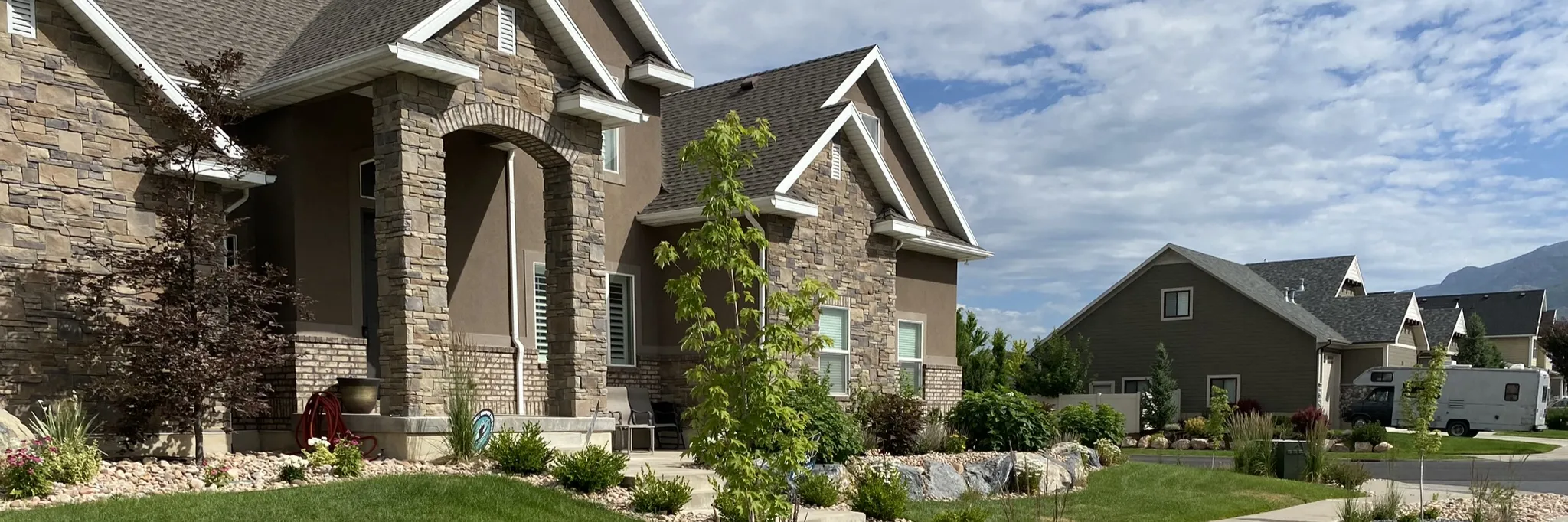 A stone house with a small lawn edged by rock beds, shrubs and young trees