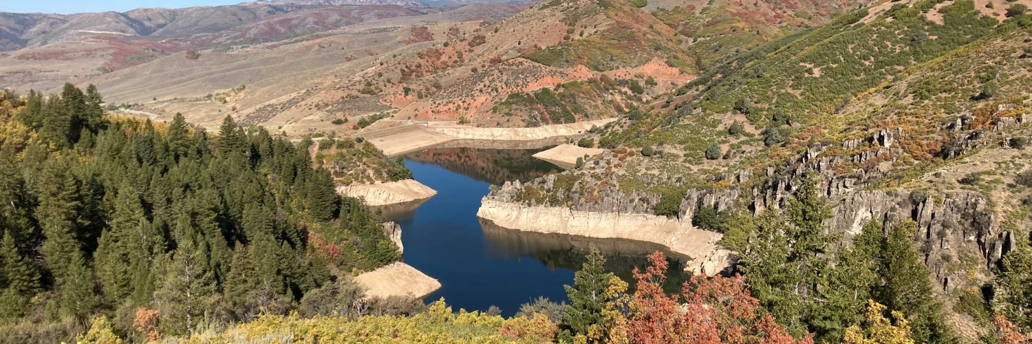 A reservoir winding through a rocky canyon, with pine trees and fall colors on the hillsides